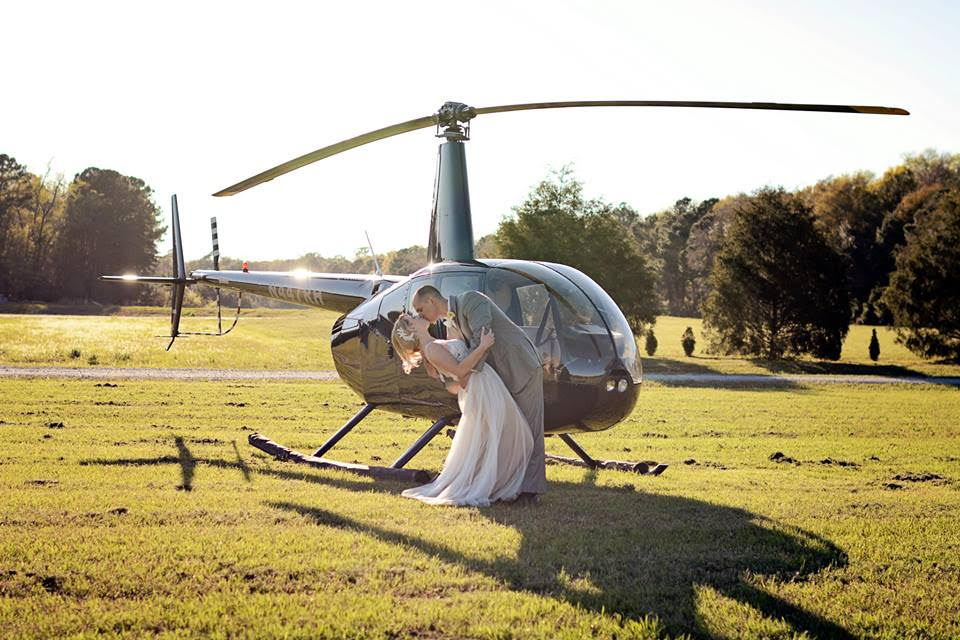 A groom dips his bride and kisses her in front of the helicopter that has come to whisk them away for their wedding night.
