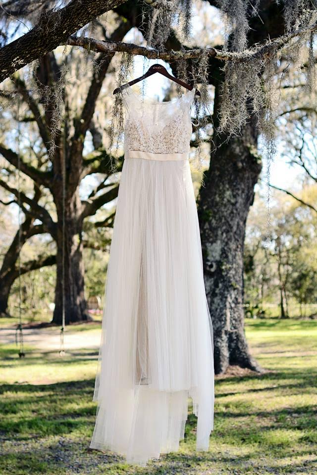 An ethereal beaded and chiffon wedding gown drifts among the branches and the moss of a grove of trees.