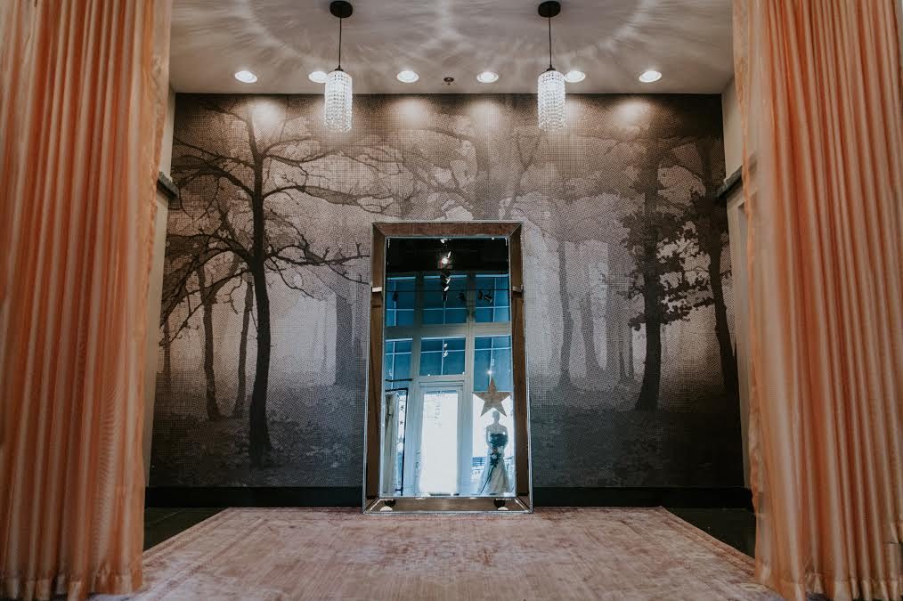 Dramatic curtains, crystal pendants, and wall art flank a large stand-alone mirror in the dressing room of Wildflower Bridal.