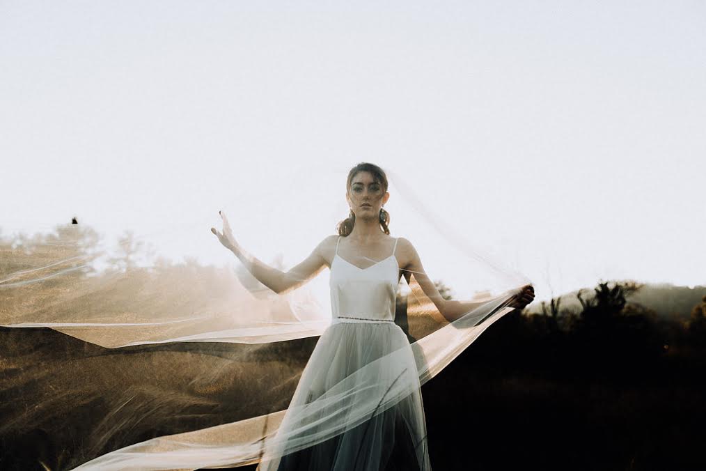 A sweeping veil wraps around a bride dressed in a simple wedding gown from Wildflower Bridal.