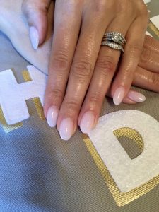 Bride folds hands to show soft, neutral manicure and her wedding ring