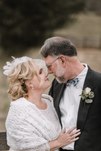 An older bride and groom nuzzle together in their wedding finery.