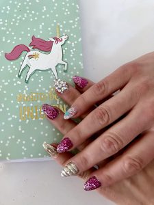 A detailed look at a unicorn manicure with a unicorn horn hail, rhinestones, and glitter.