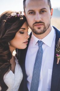 Brunette bride wearing a floral hair comb nuzzles into her groom's shoulder.