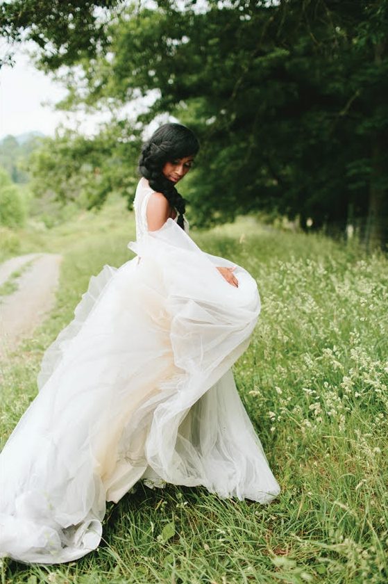 Bride in taffeta wedding gown twirls her skirt in the grass with her braided hairstyle thrown over her shoulder.