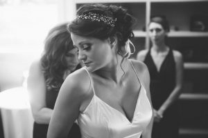 Bride wears a jeweled headband while her bridesmaids help her get dressed