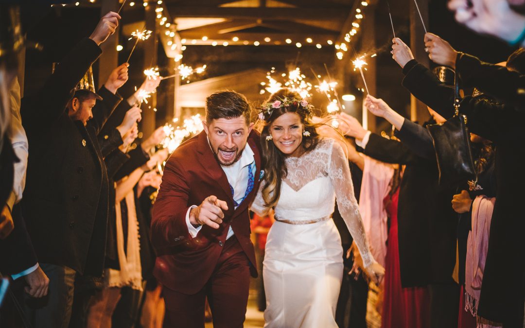 Bride and groom look at the camera as they run through a tunnel of sparklers during their wedding exit.