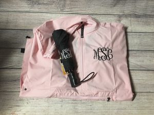 A pink raincoat with black stitched monogram and a coordinating black umbrella with a white stitched monogram by Southern Chic Boutique.