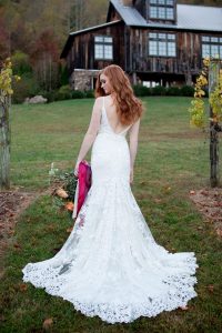 A bride looks over her shoulder as the camera photographs her lovely sleeveless lace gown from the back.