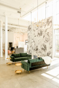 View of Engaged Asheville event space featuring white walls, floral accent wall and plush green couches.