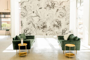 View of Engaged Asheville event space featuring white walls, floral accent wall and plush green couches.